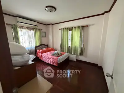 Cozy bedroom with wooden flooring and natural light, featuring a single bed and green curtains.
