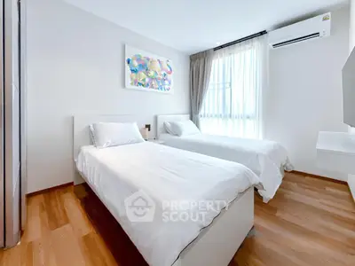 Modern bedroom with twin beds, wooden flooring, and bright natural light.