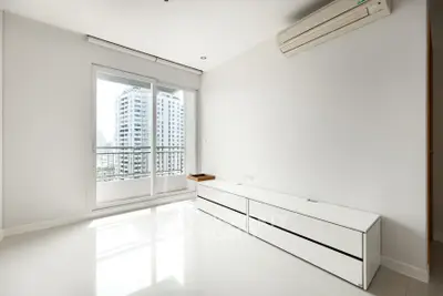 Spacious modern living room with large windows and city view, featuring sleek white furniture and air conditioning.