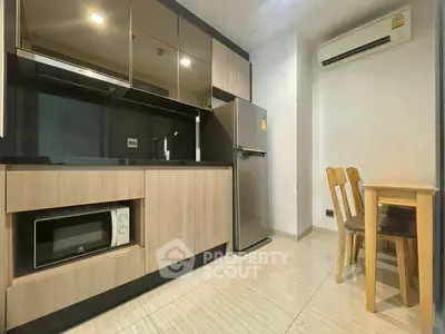 Modern kitchen with sleek cabinetry, stainless steel fridge, and cozy dining area in a stylish apartment.