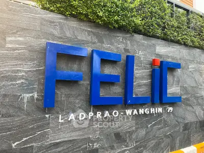 Modern building entrance with stylish signage and lush greenery, showcasing urban elegance.