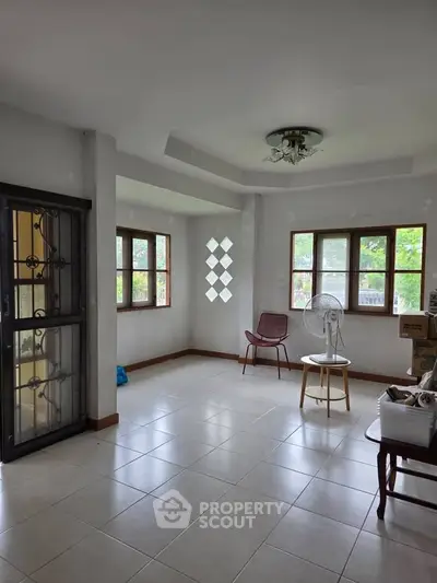 Spacious living room with natural light and tiled flooring, featuring large windows and modern decor.