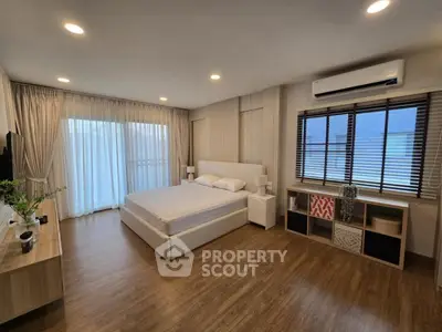 Spacious modern bedroom with wooden flooring and natural light, featuring a large bed and stylish decor.