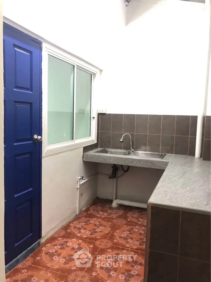 Charming kitchen with tiled floor and modern sink, featuring a vibrant blue door and ample counter space.