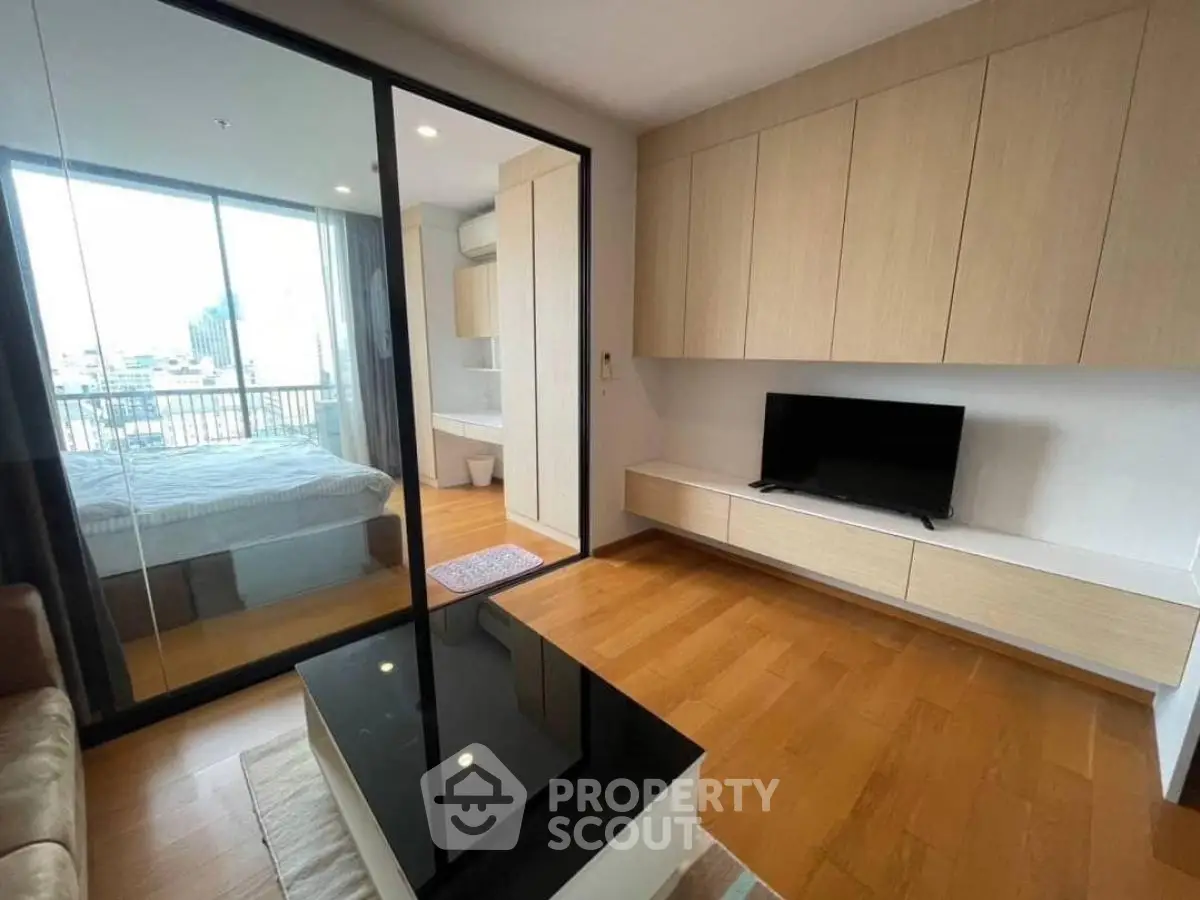 Modern living room with sleek wooden cabinets and glass partition to bedroom