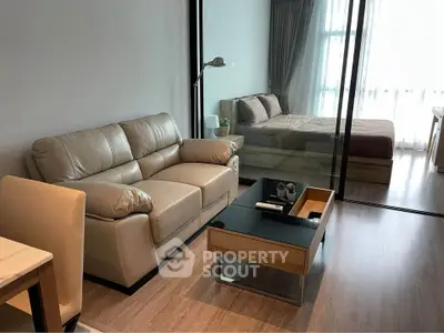 Modern living room with glass partition leading to a cozy bedroom, featuring stylish furniture and natural light.