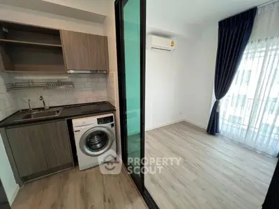 Modern apartment with compact kitchen and washing machine, featuring a bright living area with large windows.