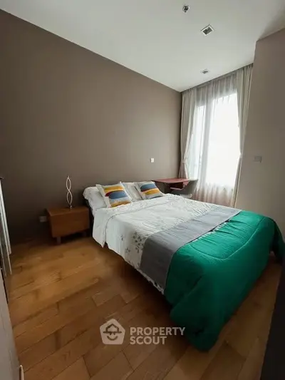Cozy bedroom with wooden flooring and natural light, featuring a comfortable bed and modern decor.