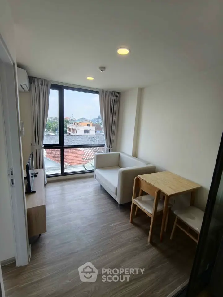 Modern living room with large window and city view, featuring cozy seating and dining area.