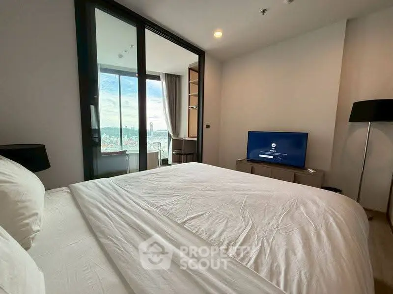 Modern bedroom with large window offering stunning city view, featuring a cozy bed and sleek TV setup.