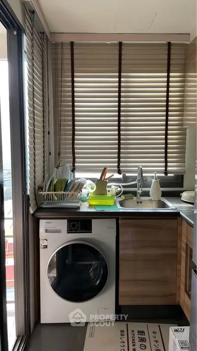 Modern kitchen with washing machine and sink, featuring sleek cabinetry and window blinds.