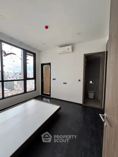 Modern bedroom with city view, dark flooring, and air conditioning unit.