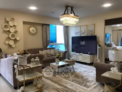 Luxurious living room with elegant decor and large TV, featuring plush sofas and a stunning chandelier.