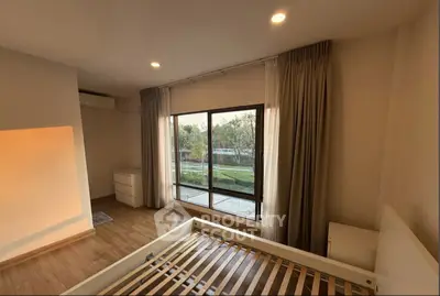 Spacious bedroom with large window offering serene garden view, wooden flooring, and modern furnishings.