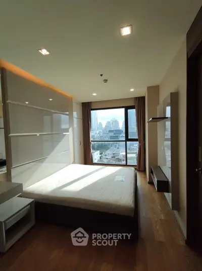Spacious bedroom with city view and modern furnishings in a high-rise apartment.