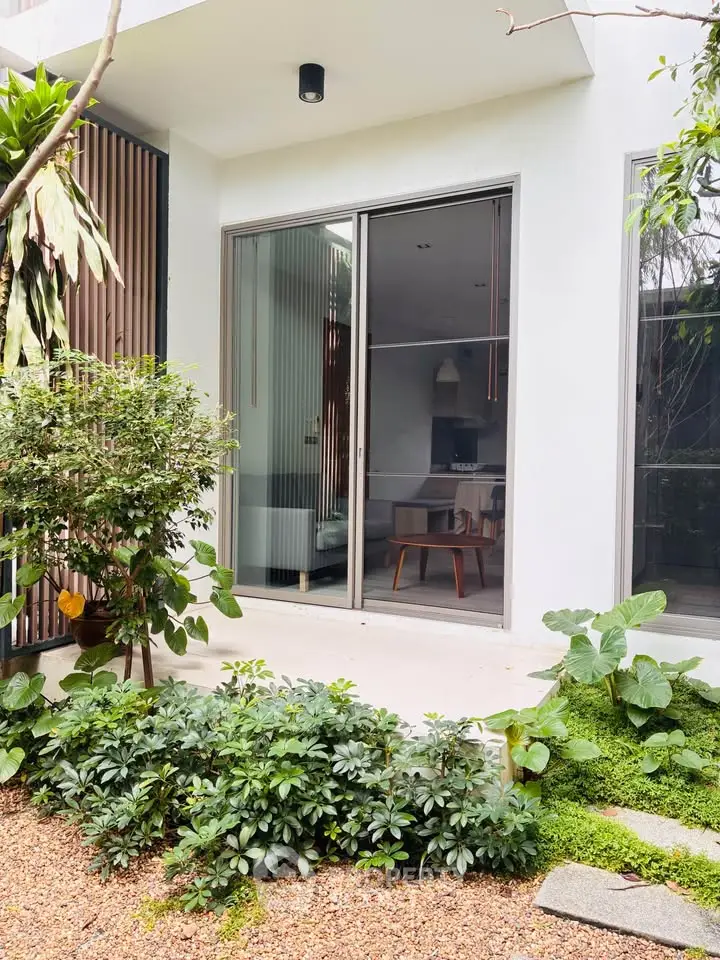 Modern home exterior with lush garden and sliding glass doors leading to stylish interior.