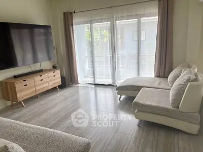 Spacious modern living room with large TV and stylish furniture, featuring a bright balcony view.