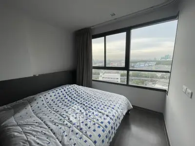 Cozy bedroom with large window offering stunning city view, perfect for urban living.