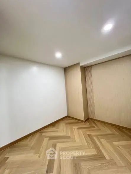 Modern empty room with elegant herringbone wood flooring and recessed lighting.