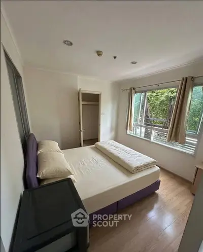 Cozy bedroom with large window and natural light, featuring a comfortable bed and wooden flooring.