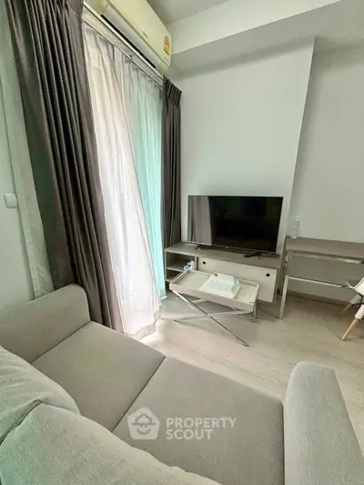 Cozy living room with modern sofa, TV, and natural light from large window.