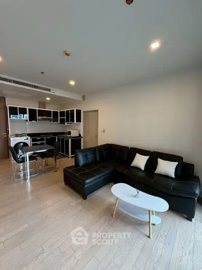 Modern open-plan living room with sleek black furniture and stylish kitchen area.