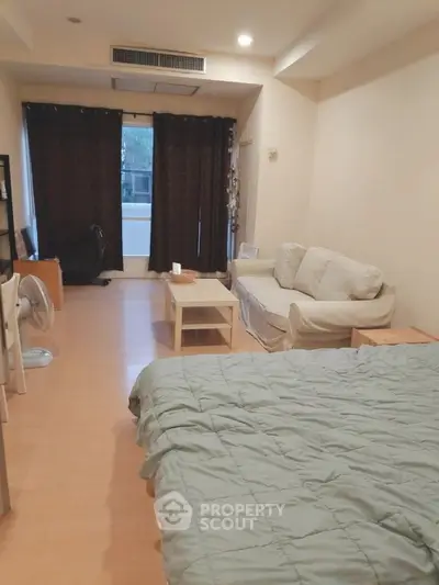 Cozy studio apartment with bed, sofa, and natural light from large window.