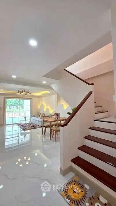 Spacious modern living room with elegant staircase and dining area, featuring bright lighting and stylish decor.