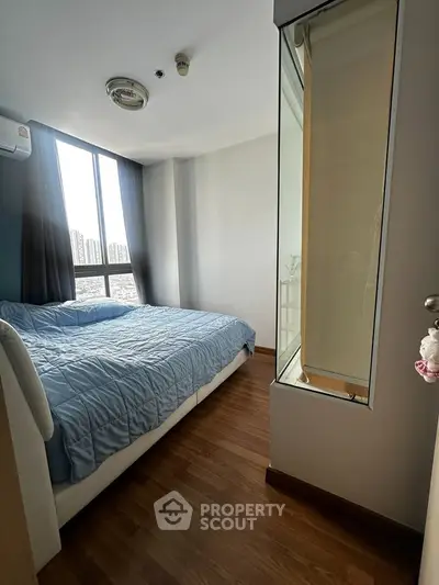 Modern bedroom with large window and wooden flooring in high-rise apartment.