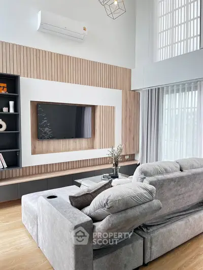 Modern living room with stylish decor and cozy gray sofa, featuring a sleek wall-mounted TV and elegant wood paneling.