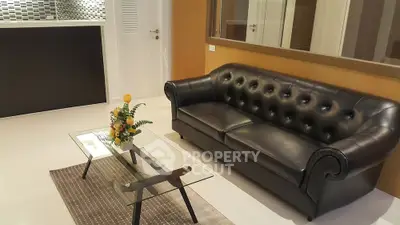 Stylish modern living room with black leather sofa and glass coffee table.