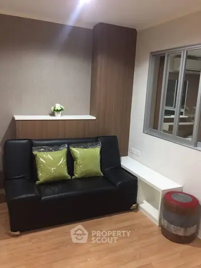 Modern living room with sleek black sofa and green cushions, featuring wooden flooring and stylish decor.
