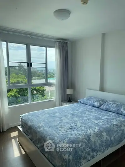 Bright bedroom with large window and blue floral bedding, offering a serene view.