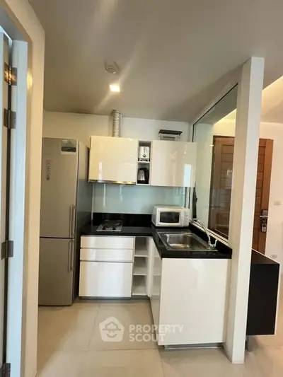 Modern compact kitchen with sleek white cabinets and stainless steel appliances.