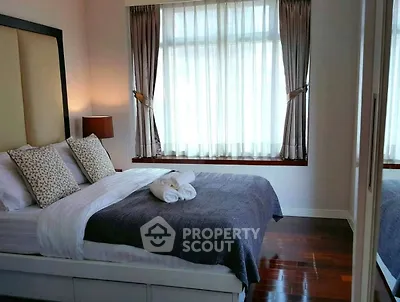 Elegant bedroom with cozy bedding and natural light through large window.