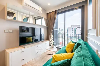 Modern living room with green sofa, large TV, and city view from balcony.