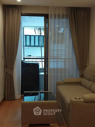 Cozy living room with modern sofa and glass coffee table, leading to a balcony with city view.