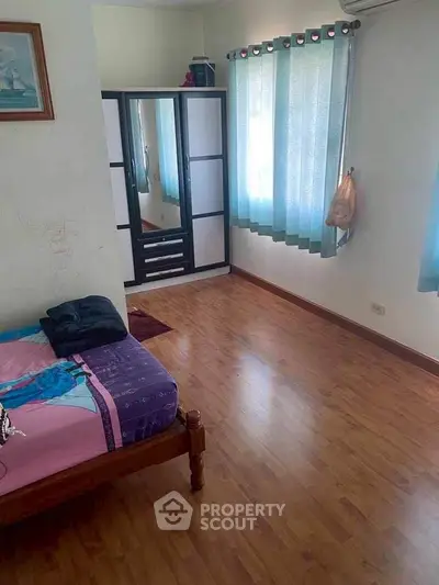 Spacious bedroom with wooden flooring and natural light