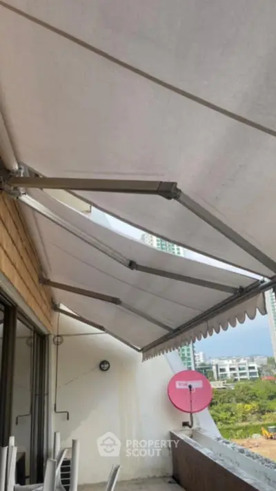 Spacious balcony with retractable awning and city view, perfect for outdoor relaxation.