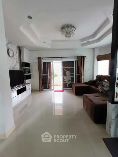 Spacious living room with elegant chandelier and modern entertainment center, featuring large windows for natural light.