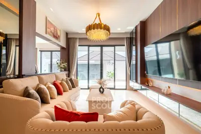 Luxurious living room with elegant chandelier and modern decor, featuring plush sofas and large flat-screen TV.