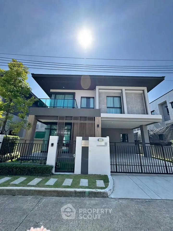 Modern two-story house with sleek design and large windows under a bright blue sky.