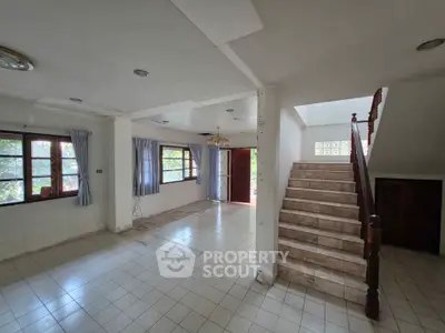 Spacious open-plan living area with staircase and large windows in a bright home.