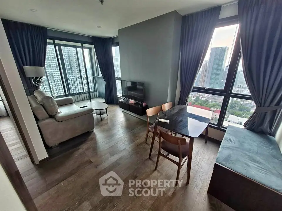 Modern living room with city view, featuring sleek furniture and large windows in a high-rise apartment.