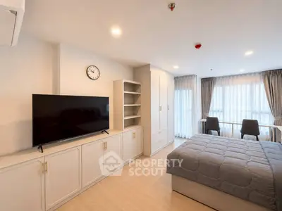 Modern bedroom with sleek design, featuring a large TV, ample storage, and natural light from wide windows.