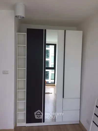 Modern bedroom with sleek wardrobe and large window offering natural light.