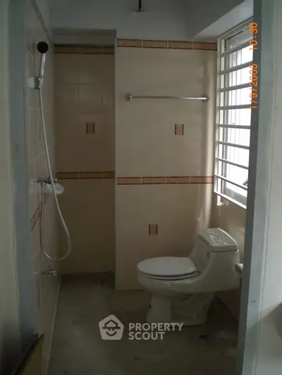 Compact bathroom with shower and toilet, featuring tiled walls and window for natural light.