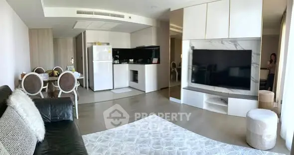 Modern living room with open kitchen, featuring sleek furniture and large TV, perfect for contemporary living.