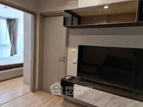 Modern living room with sleek TV setup and view into cozy bedroom.