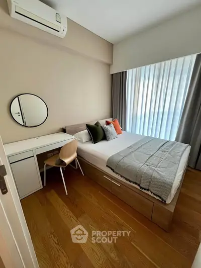 Modern bedroom with stylish decor, featuring a cozy bed, wooden flooring, and natural light from large windows.